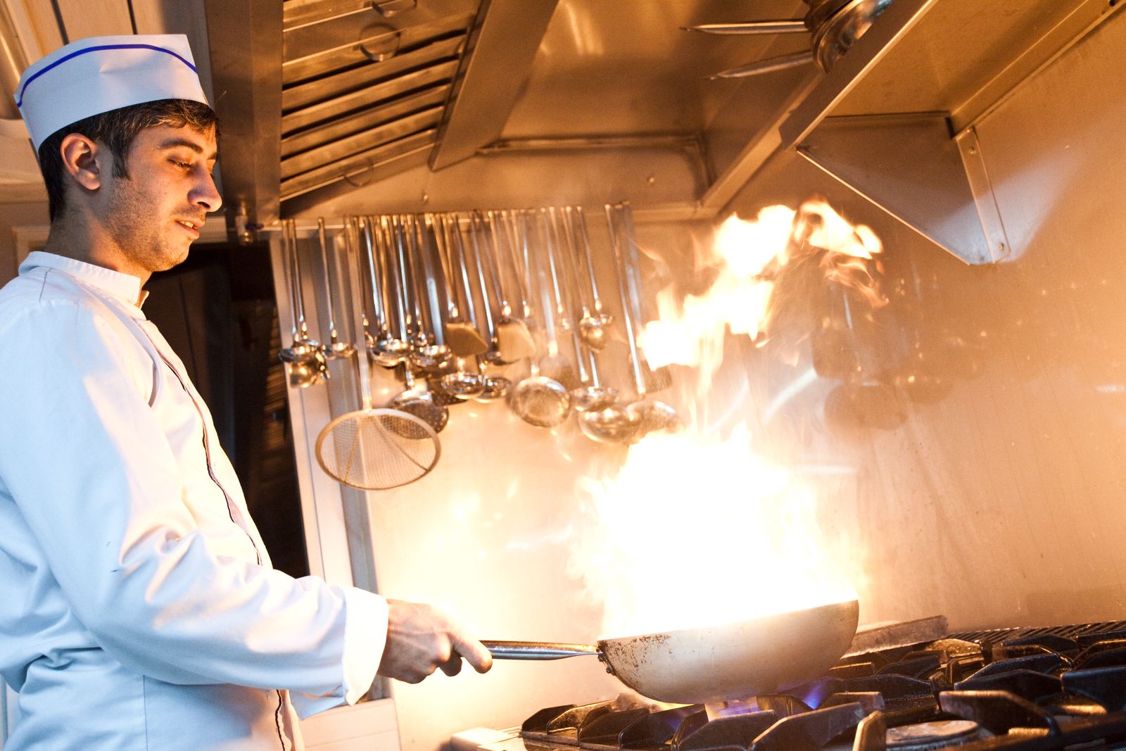 Chef in white flaming a pan in a professional kitchen