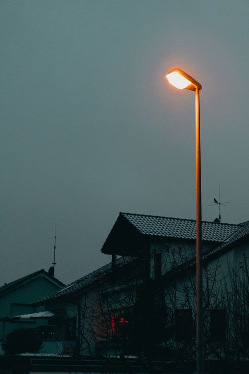 Free A streetlight casts a warm glow over snow-dusted rooftops on a calm evening. Stock Photo