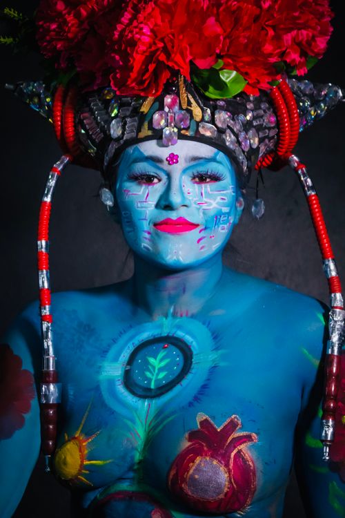 Free Captivating portrait of a woman in blue body paint with intricate headgear adorned with vibrant flowers. Stock Photo