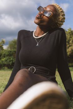 Elegant black woman in sunglasses and pearls posing in a sunny outdoor setting.