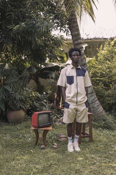 Stylish man in casual summer outfit poses outdoors with retro television.