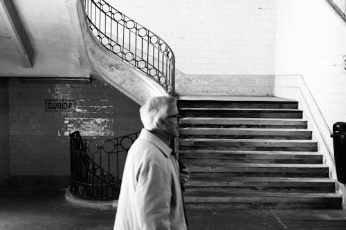 Grayscale Photography of Man Walking Near Staircase