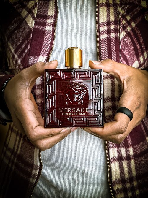 Free Hands holding a Versace Eros Flame perfume bottle against plaid clothing backdrop. Stock Photo