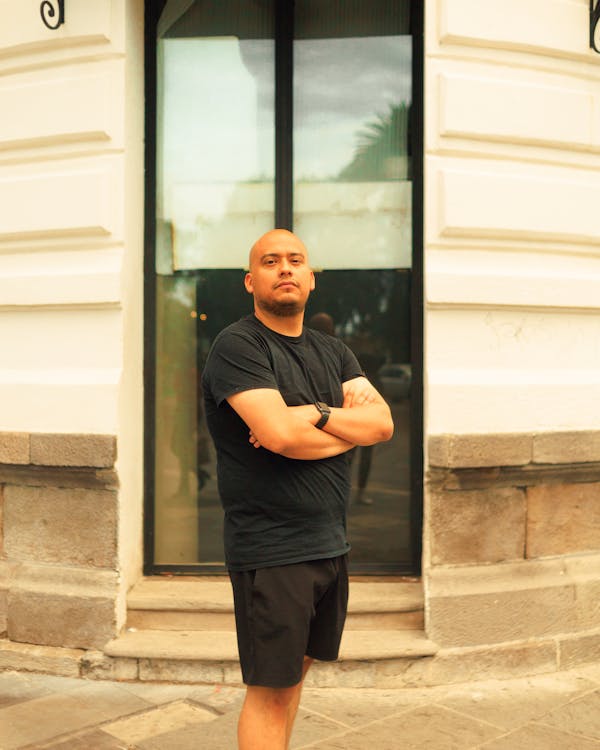 Bald Man in Black Shirt is Standing Near Glass Window