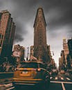 一辆黄色出租车在繁忙的街道上行驶，背景是暴风雨天空下的熨斗大厦