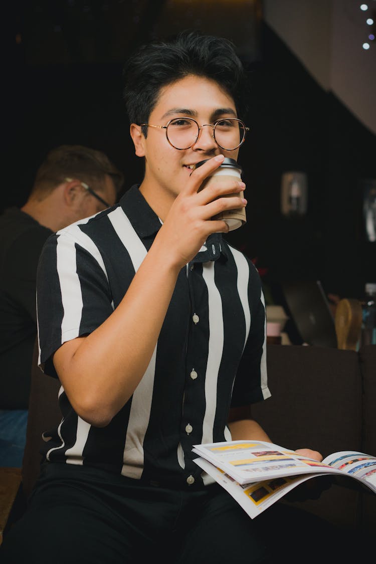 Man In Black And White Striped Polo Holding A Paper Cup And Magazine 