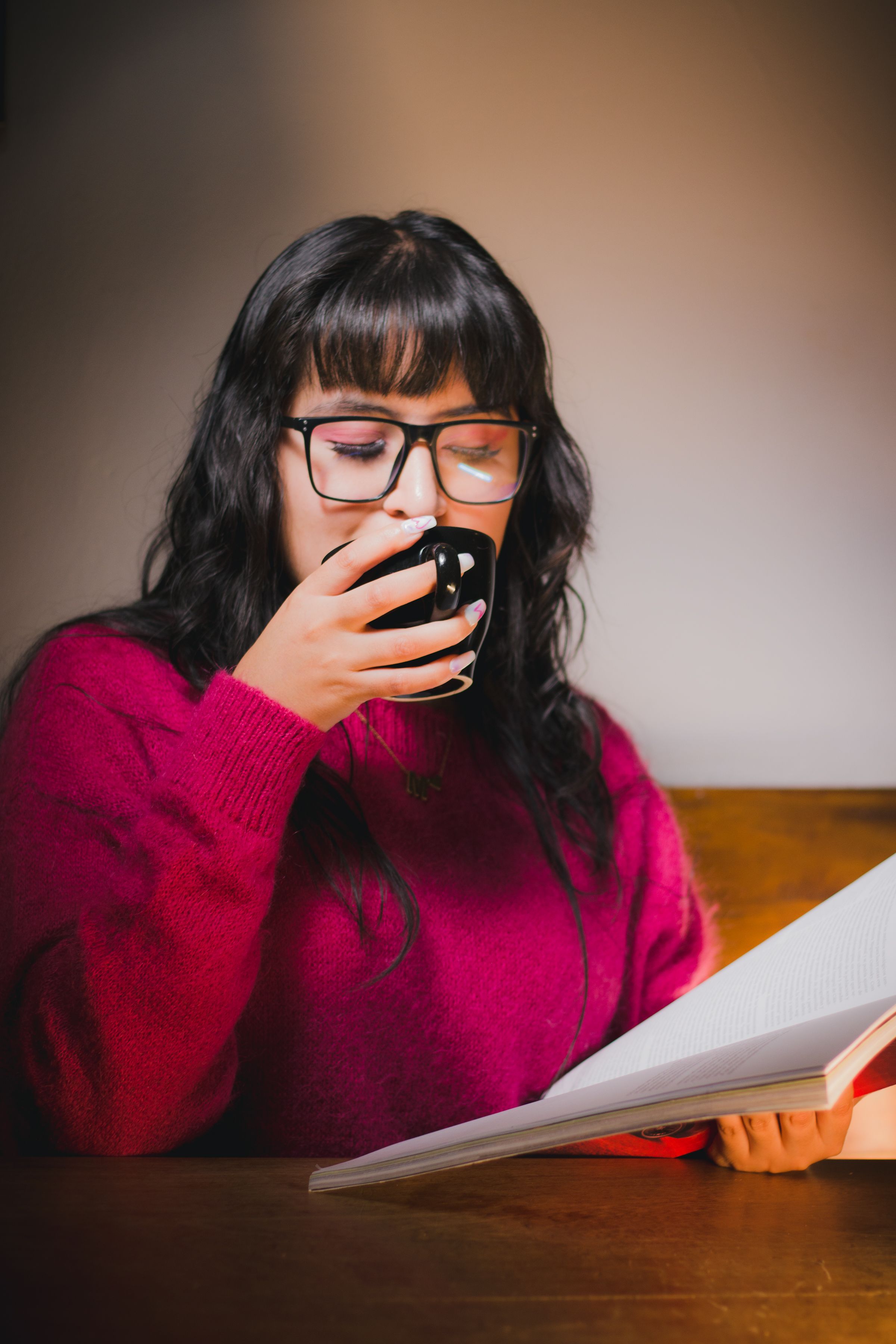 A woman in a purple sweater enjoys coffee and reading indoors. Warm and cozy atmosphere.