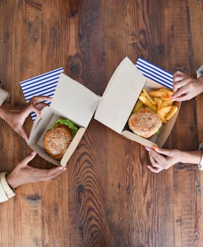 Aerial view showing two people enjoying burgers and fries on a rustic wooden table.