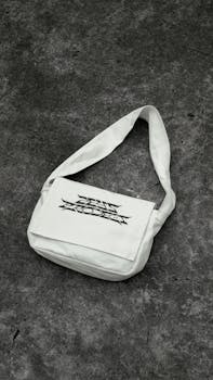 Stylish white shoulder bag with urban design on a textured concrete surface, perfect for contemporary fashion enthusiasts.