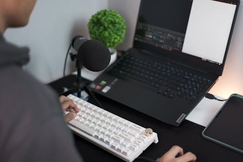 Man Sitting Behind His Desk with a Laptop, Keyboard and a Microphone 