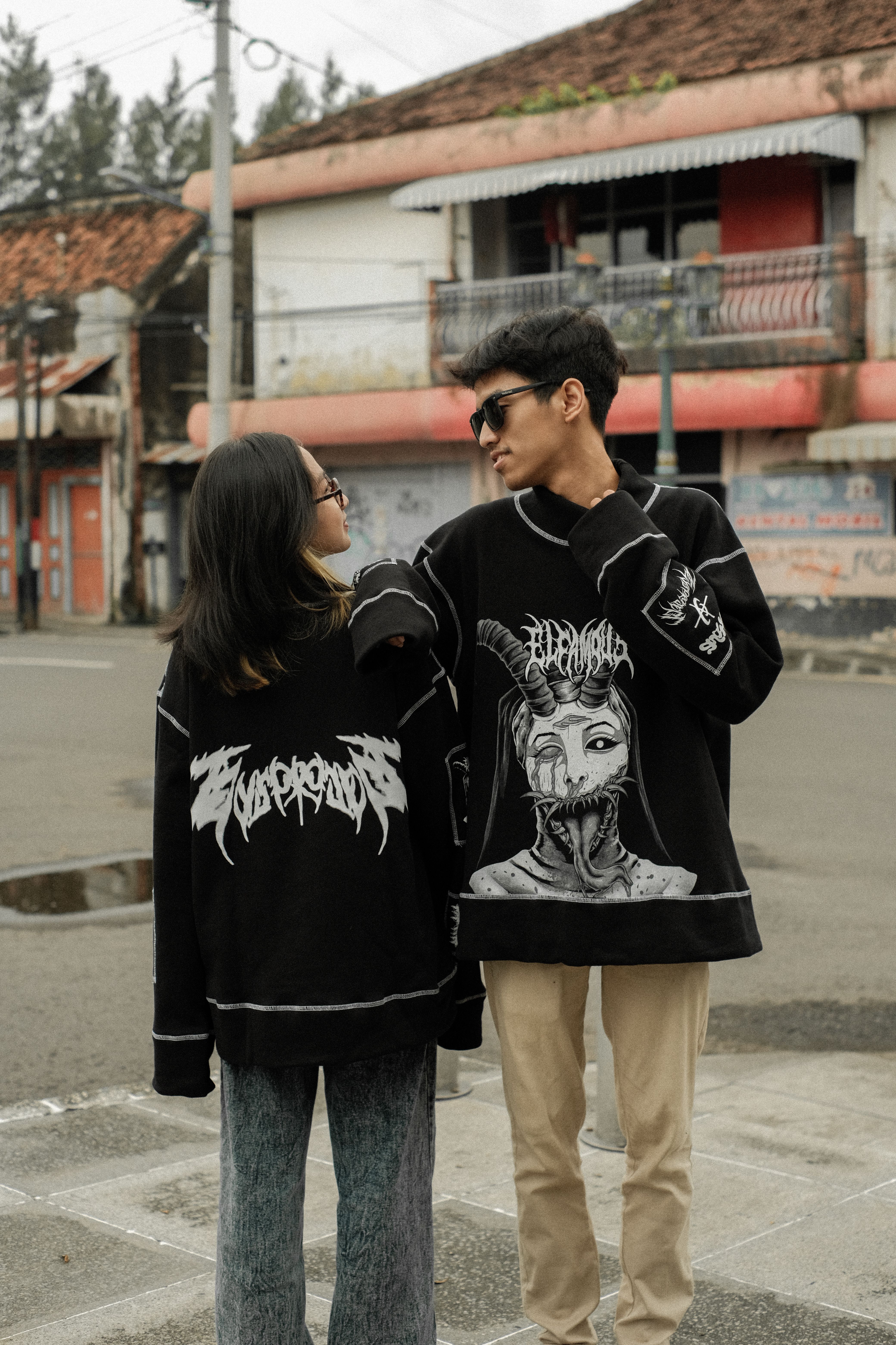 A stylish couple poses in urban streetwear on a city street, showcasing modern fashion.