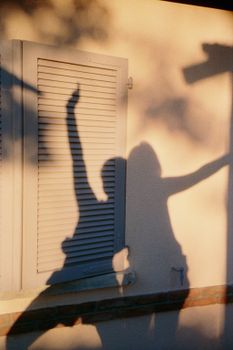 Silhouettes of people casting artistic shadows on a sunlit wall with a shuttered window.