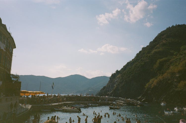 People Swimming On Lake Near The Mountains