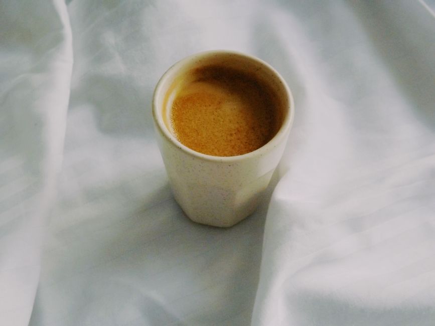 A close-up view of a coffee cup with frothy espresso on soft white fabric.