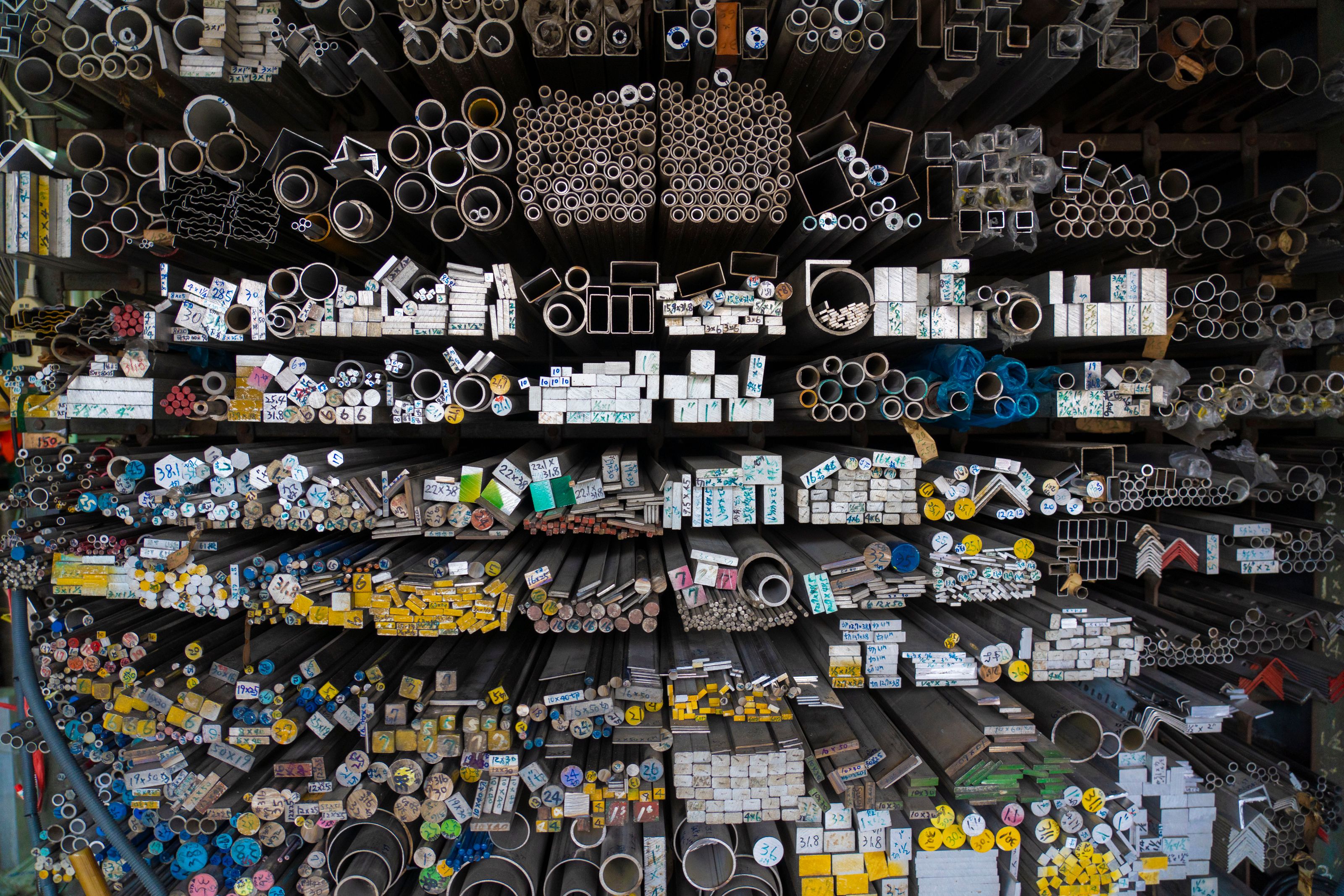 Diverse collection of stacked metallic pipes and rods in a warehouse display.