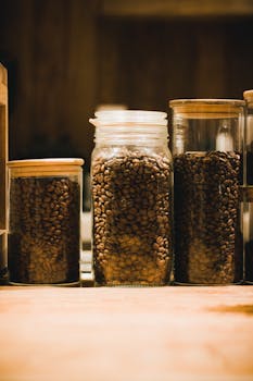 A warm-toned close-up of coffee beans stored in glass jars, evoking a cozy atmosphere.
