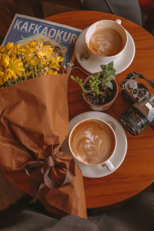 Free Warm, artistic setting with cappuccinos, flowers, and vintage camera. Stock Photo