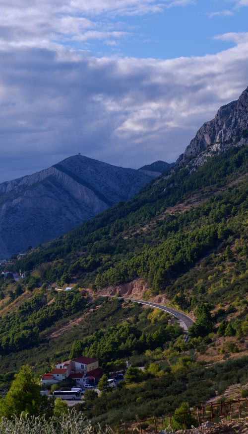 Free Explore a scenic mountain road surrounded by lush greenery and picturesque village views. Stock Photo