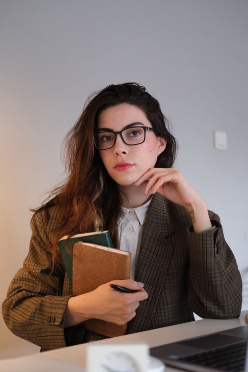 Free Portrait of a woman in a plaid blazer holding books, creating an academic atmosphere. Stock Photo