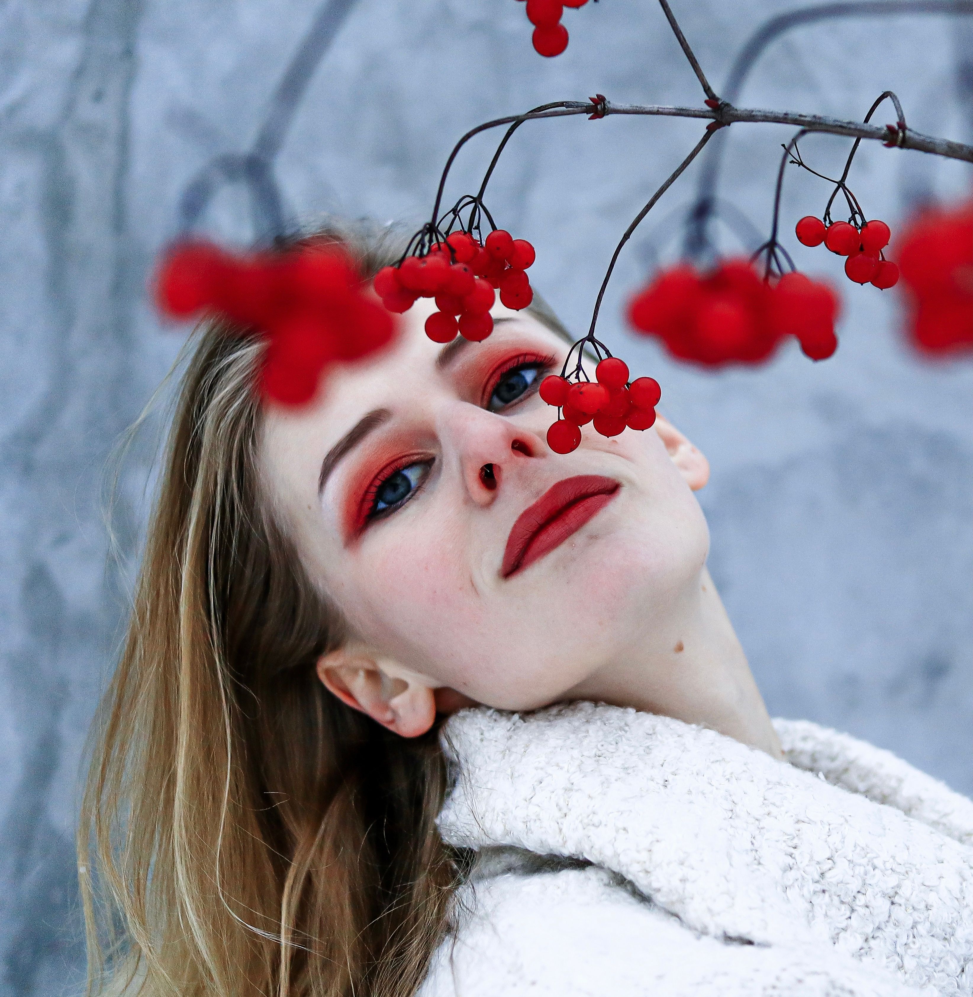 A woman in winter attire poses with red berries against a snowy backdrop.