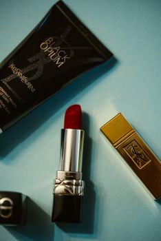 Close-up of Yves Saint Laurent Black Opium perfume and red lipstick on blue background.