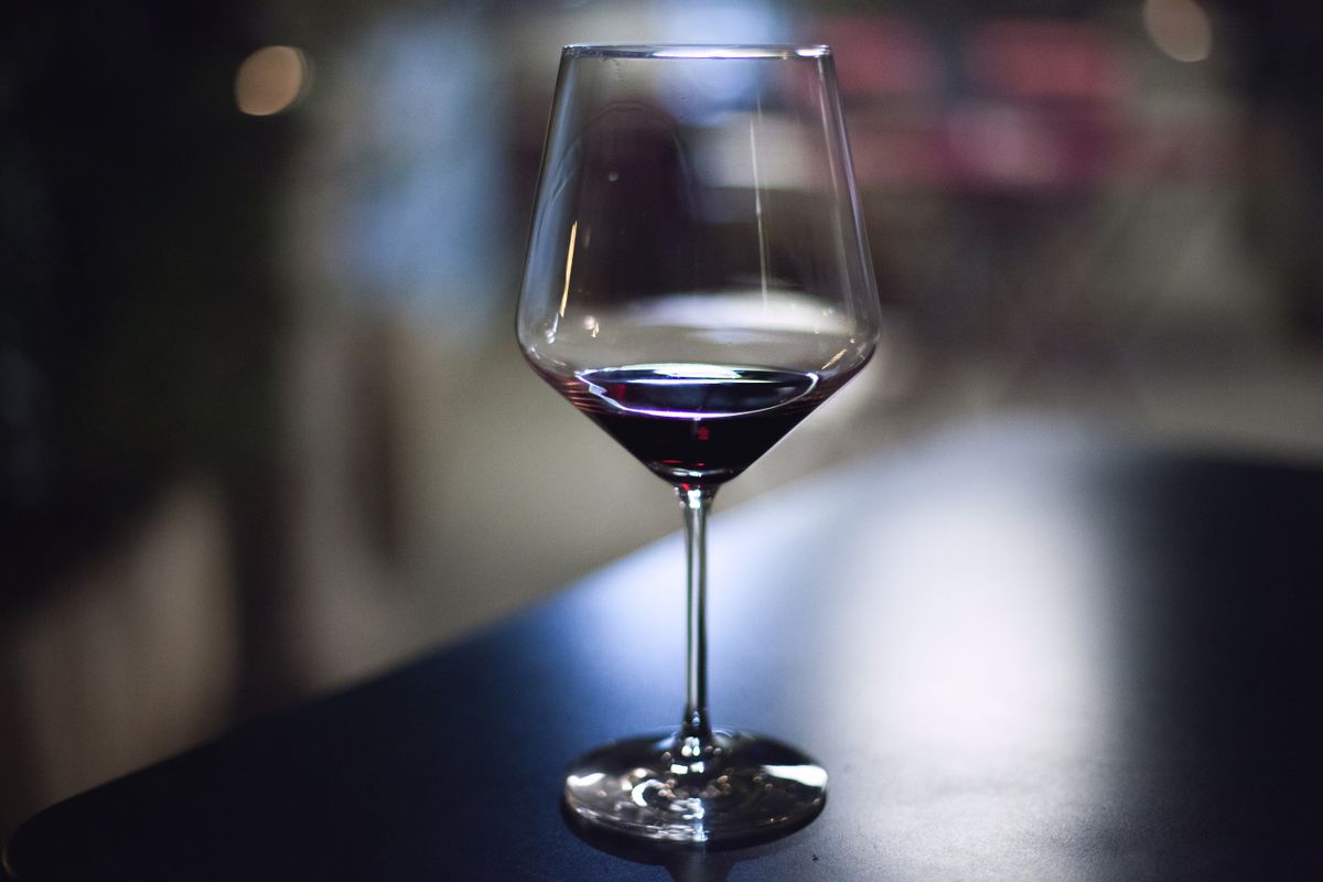 A close-up of a wine glass filled with red wine on a dark table in an indoor setting.