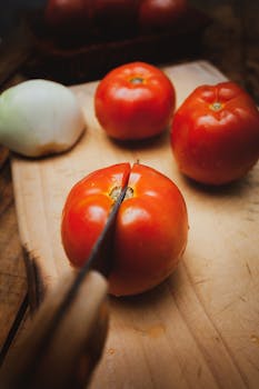 Close-up of ripe tomatoes being sliced on a wooden board with a knife, ideal for cooking themes.