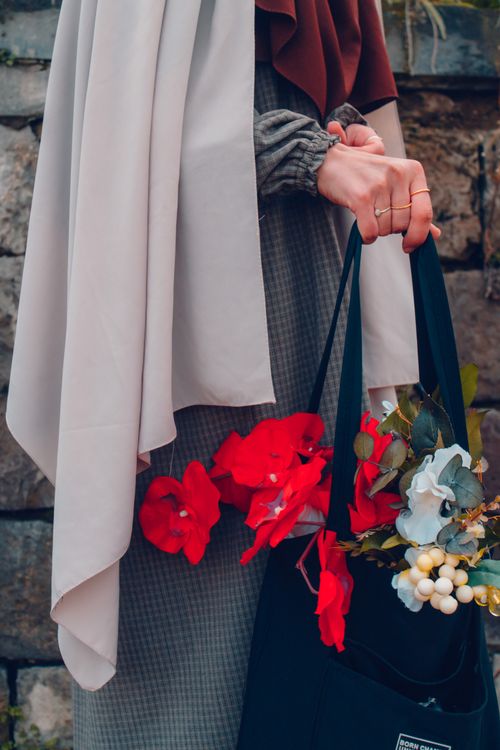 Free Stylish woman holding a bag filled with vibrant red and white flowers against a stone background. Stock Photo