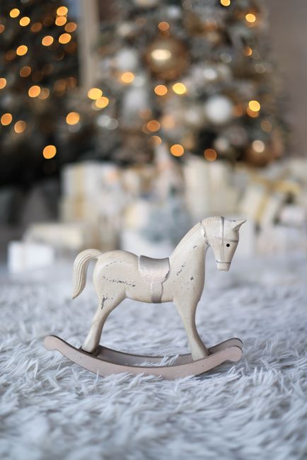 Charming rustic wooden horse figurine in front of a Christmas tree with bokeh lights.