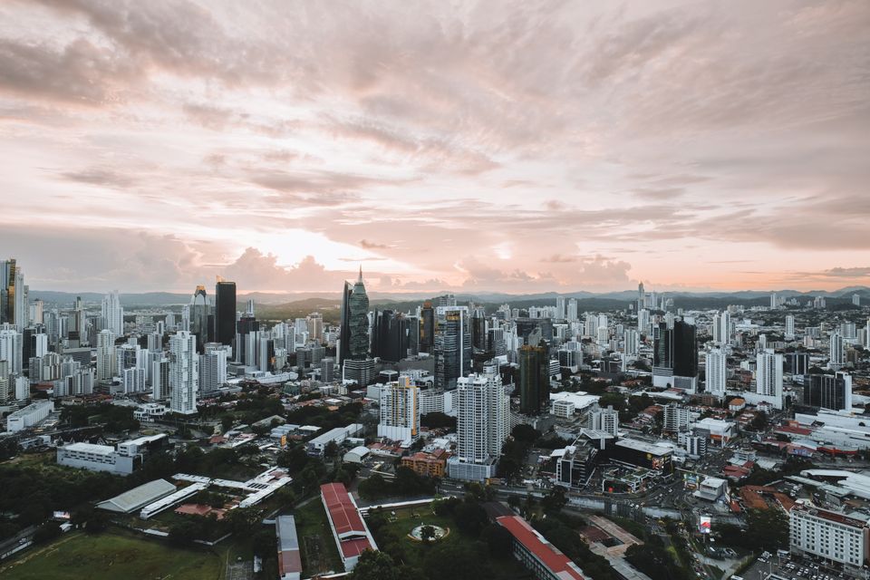 Wide aerial view of a dense city skyline under a pink and orange sunset sky