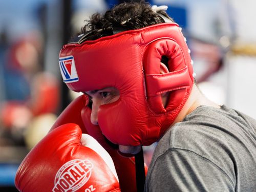 Free A boxer wearing red gloves and headgear focuses intensely during training indoors. Stock Photo