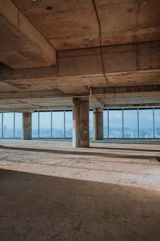 Spacious unfinished skyscraper interior with city skyline views through large windows.