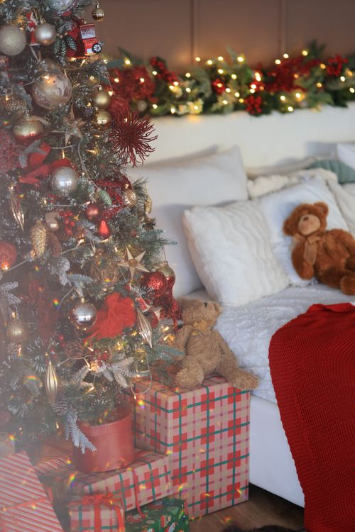Free Warm and festive bedroom featuring a beautifully decorated Christmas tree with gifts beside a comfy bed. Stock Photo