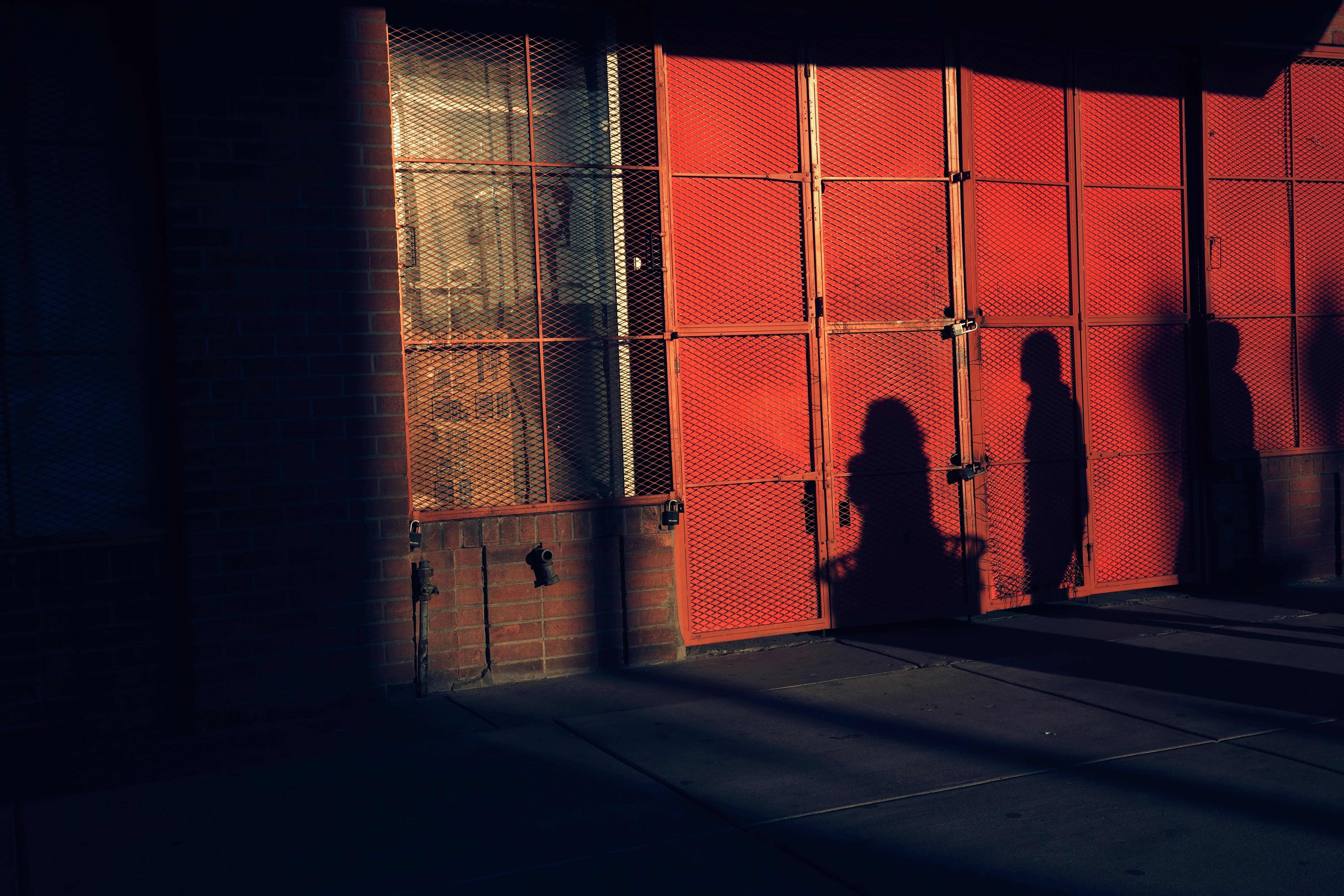 Silhouettes and shadows cast on a red urban wall at sunset, creating a moody ambiance.