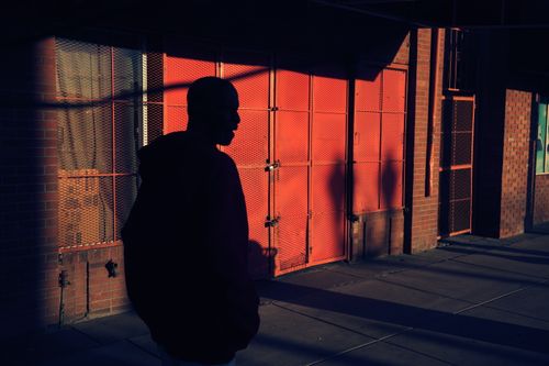 Free Silhouette of a person walking along an urban sidewalk in dramatic lighting, creating strong shadows. Stock Photo
