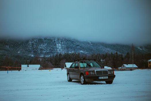 A retro car parked in a snowy mountain setting, surrounded by fog and winter scenery.