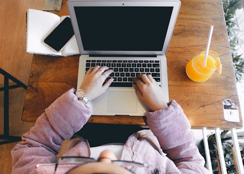 High angle view of a woman using a laptop on a wooden table with orange juice and a smartphone.