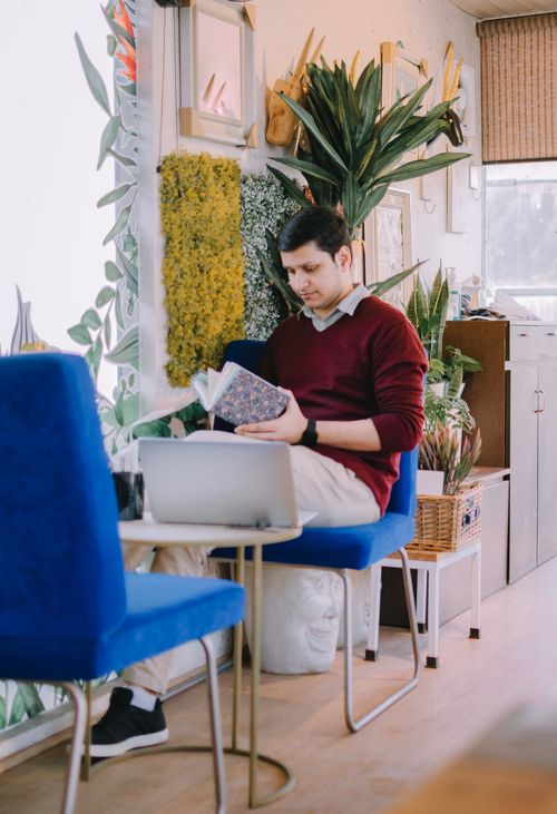 Free A young man with short hair reading in a bright, plant-filled cafe setting. Stock Photo