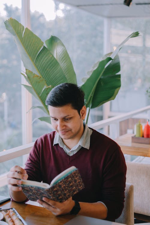 A Man Reading a Book Near Green Leaves