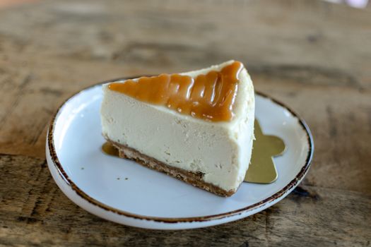 Close-up of a delicious cheesecake slice with caramel topping on a rustic plate.