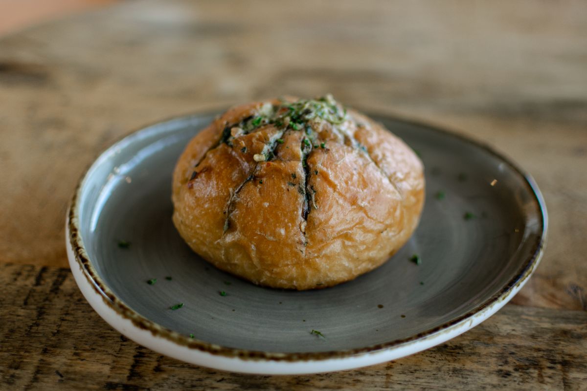 Round crusty bread roll cut in a crosshatch and filled with green herb garlic butter