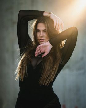 Brunette woman in black long sleeves poses elegantly with dramatic backlighting.