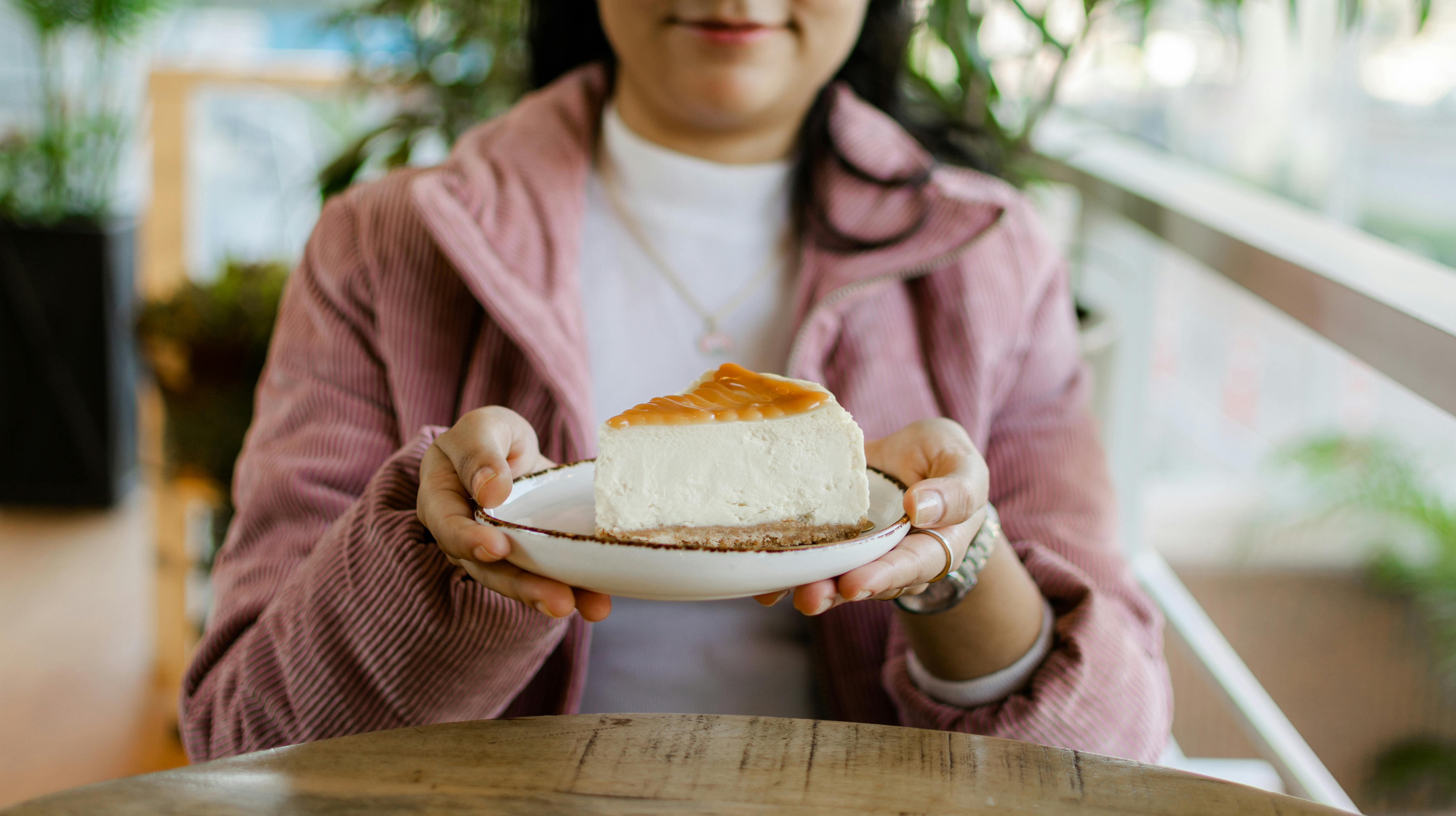 Close-up of a woman holding a plate with a slice of creamy cheesecake in a cozy cafe.