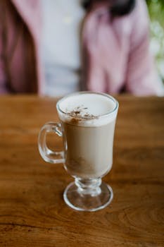 Close-up of a creamy cappuccino in a glass cup on a wooden table, perfect for a cozy coffee moment.