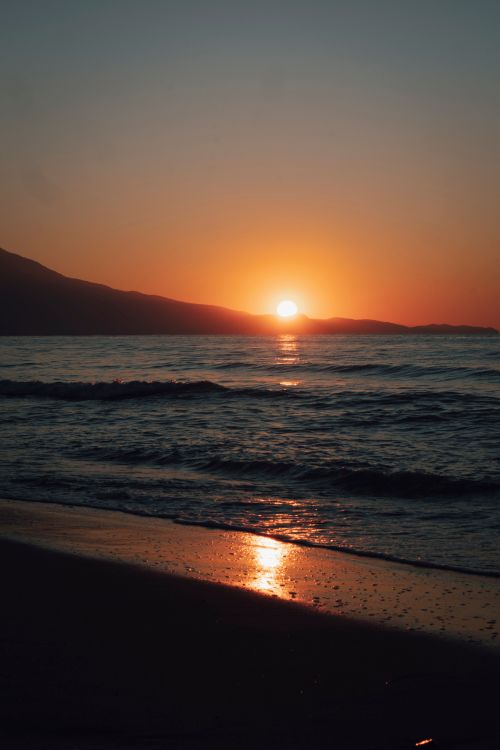 Free Peaceful sunset scene with waves and glowing sky at a sandy beach. Perfect for coastal tranquility themes. Stock Photo