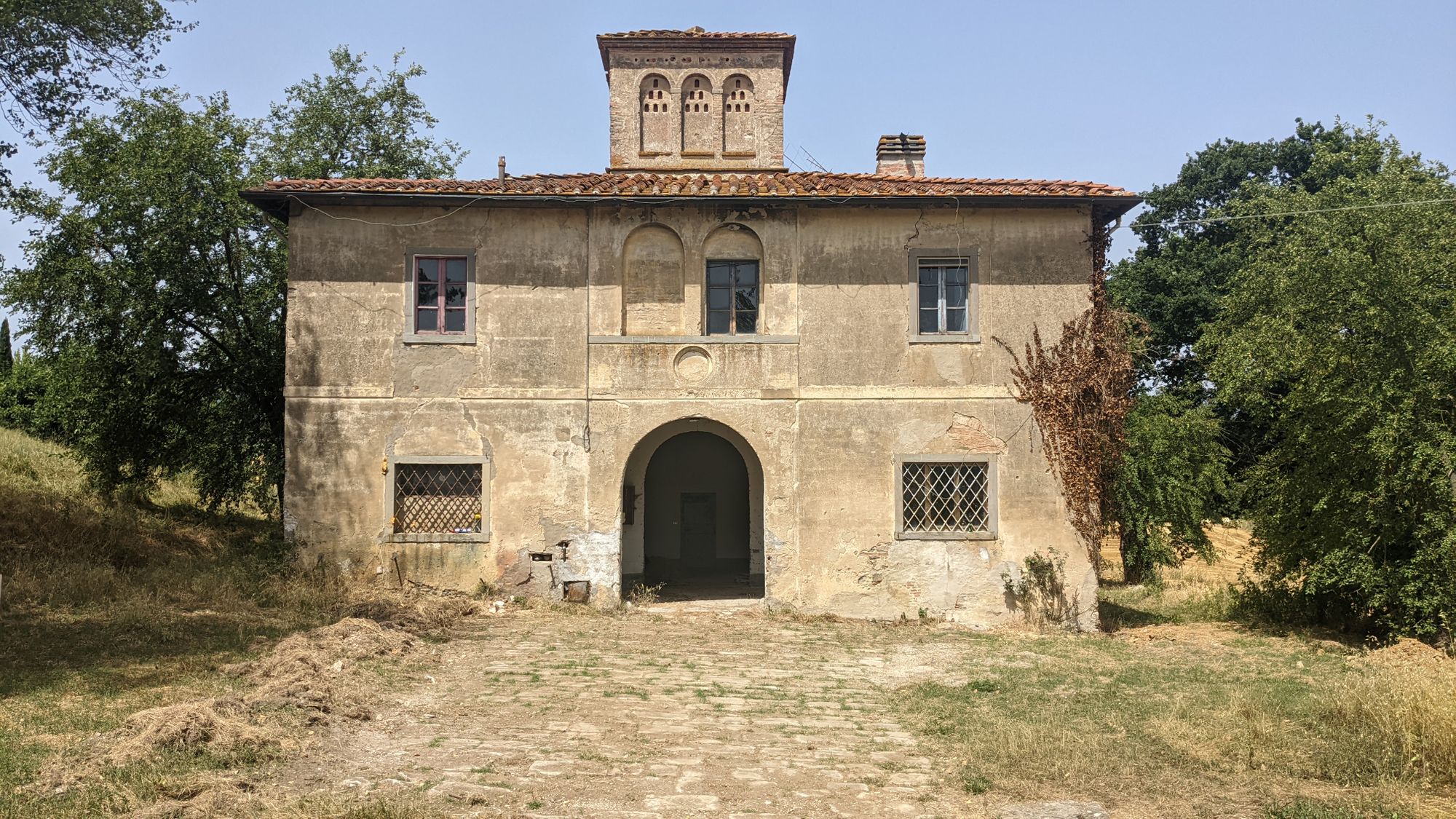A rustic Tuscan farmhouse with a charming archway under the summer sun.