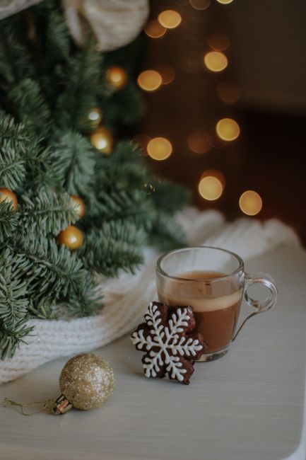 Warm cup of coffee with snowflake cookie and Christmas tree in a festive, cozy setting.