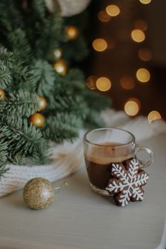Warm coffee with snowflake cookie and Christmas ornaments near a pine tree.