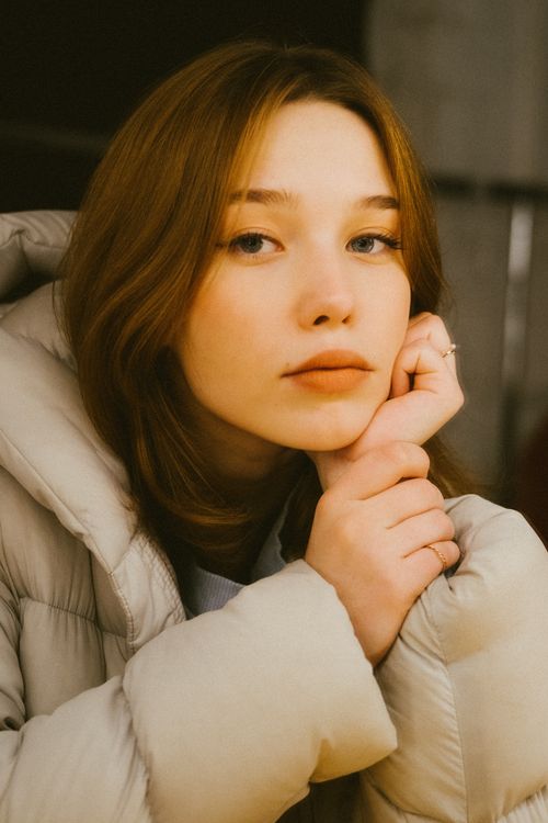 Free Portrait of a young woman with long hair wearing a light down jacket indoors. Stock Photo