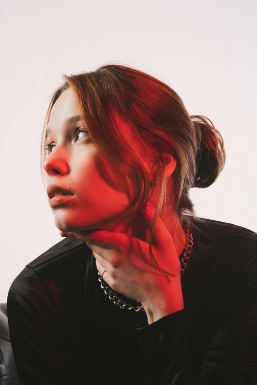Free Portrait of a young woman with dramatic red lighting and thoughtful expression. Stock Photo